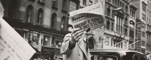 Old black and white image of a man holding a newspaper on a New York street