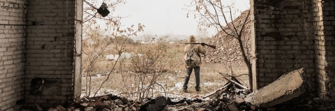 A lone soldier with a gun stands in a desolate landscape