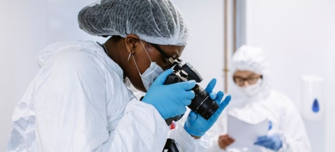 Side profile image of a student wearing a crime scene investigation uniform, including a hair net and blue gloves taking a photo  in our Crime scene simulation facilities