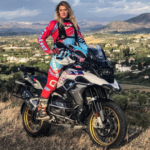 Vanessa Ruck wearing red motor suit sitting on motorbike looking to camera with scenic background