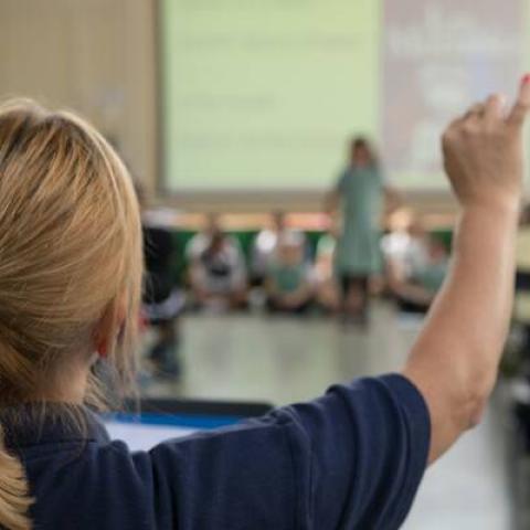 Teacher in classroom raising her hand