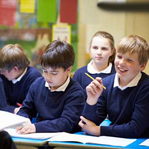 School children in a classroom, sitting at a desk with workbooks
