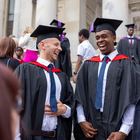 Two students laughing together on graduation day outside Portsmouth Guildhall