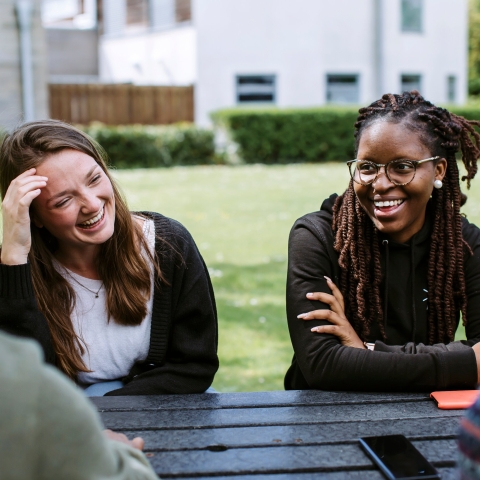 Students smiling in sun at picnic table outside of the Students' Union