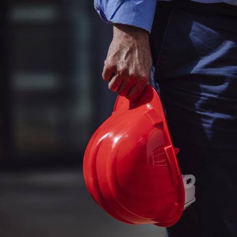 Male worker holding red hard hat at building site
