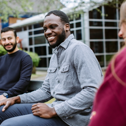 Three students sat together outside university building laughing