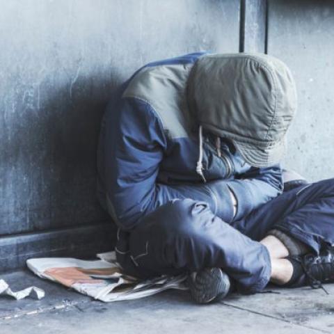 Homeless person sitting on sidewalk with head down