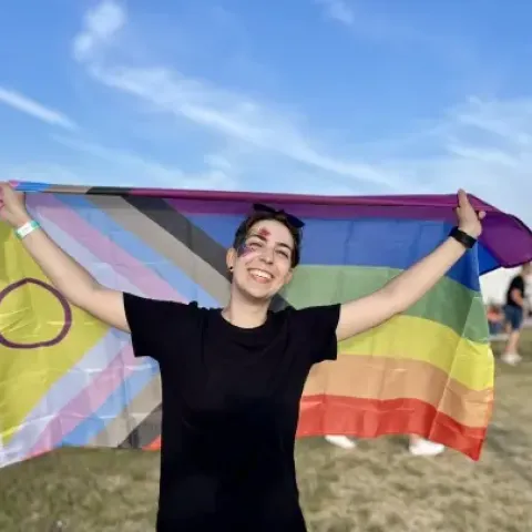 Mar smiling, holding a LGBTQ+ flag at Pride Festival