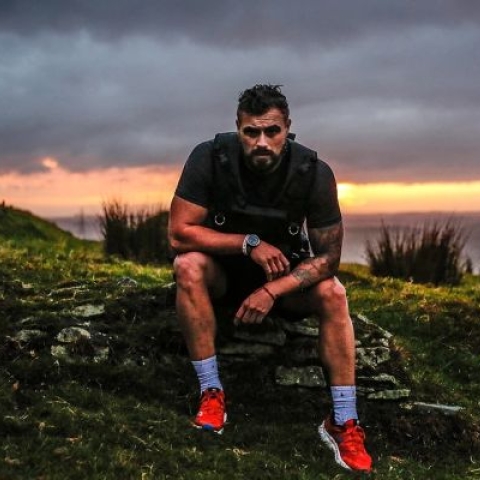 Josh Llewellyn-Jones in running clothes sitting on a mountain
