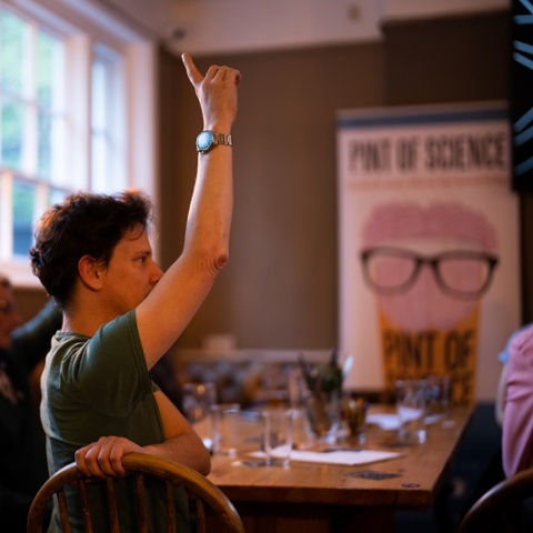 A man raising his hand in a pub with a Pint of Science sign in the background