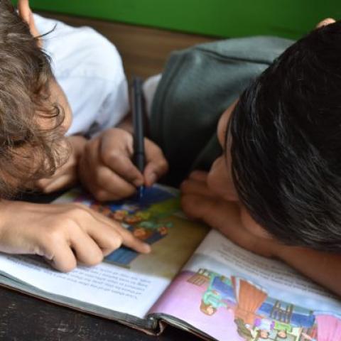 Two boys reading and writing in a book.