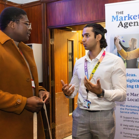 Two men talking in front of a Marketing Agency banner
