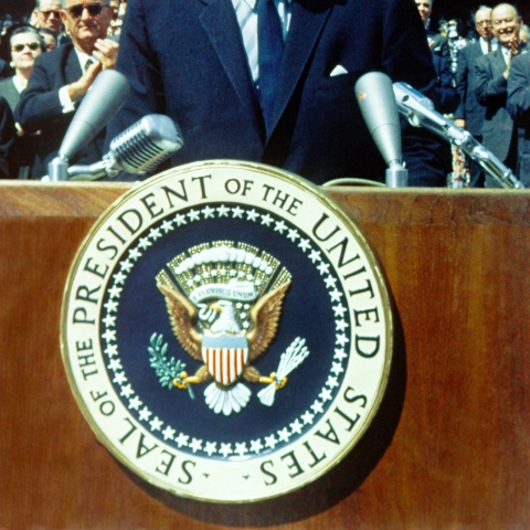 JFK standing on stage in front of podium - Photo by History in HD on Unsplash