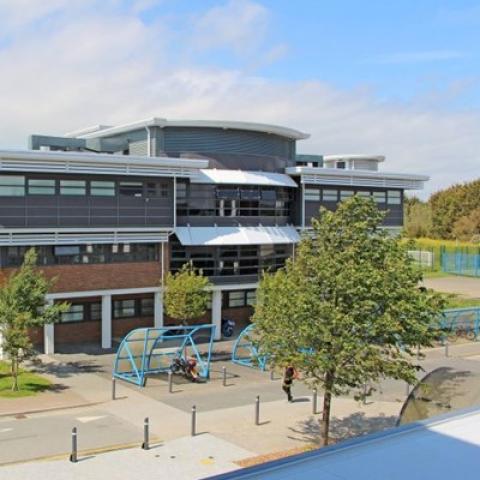A modern building with bike storage and trees outside, part of Isle of Wight College