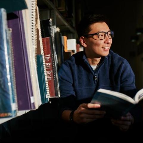 Male student smiling and browsing books in library