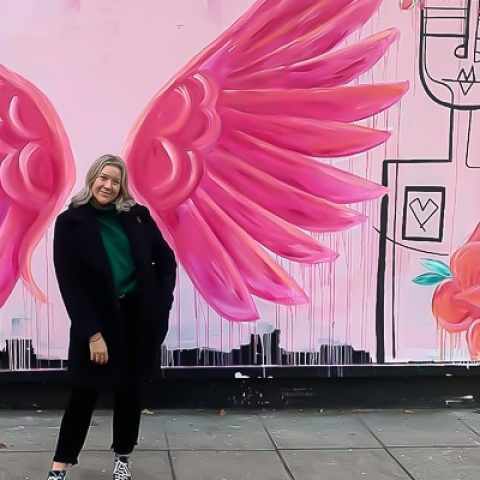 Sam Watkins standing in front of a wall with pink wings painted on it