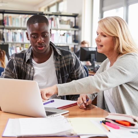 A teacher with a student, both looking at a laptop
