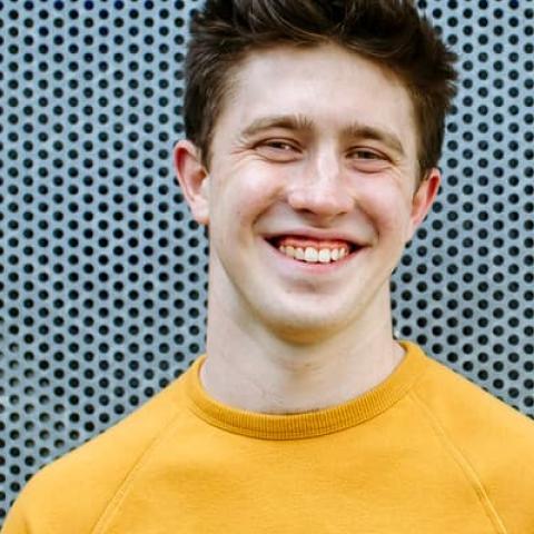 Smiling male student stood outside in yellow jumper