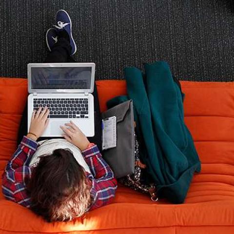 Student studying with laptop on orange sofa
