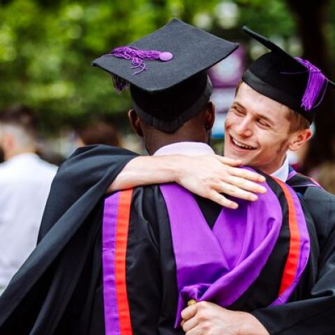 Two male students in graduation gowns hugging