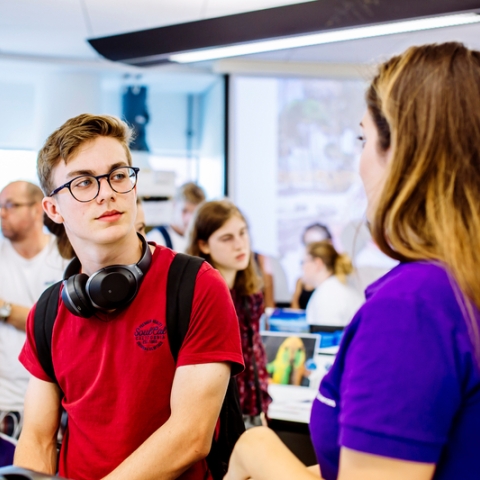 A male with glasses and headphones talking to a student ambassador