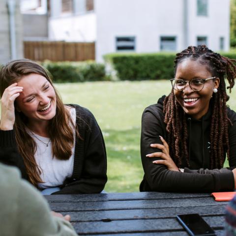 Students smiling in sun at picnic table outside of the Students' Union
