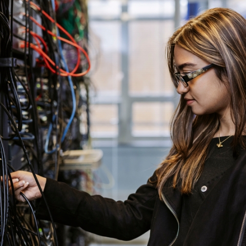 Student adjusts ethernet cables on server wall in Technology Facilities