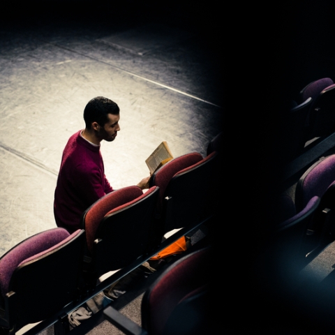 Man reading a play in dimly-lit theatre space