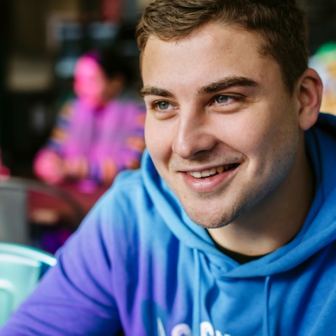 A male student smiling whilst wearing a blue hoodie