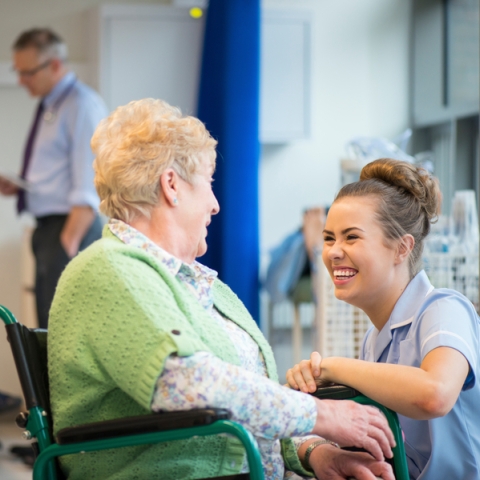 Female nurse speaking to elderly female patient in wheelchair