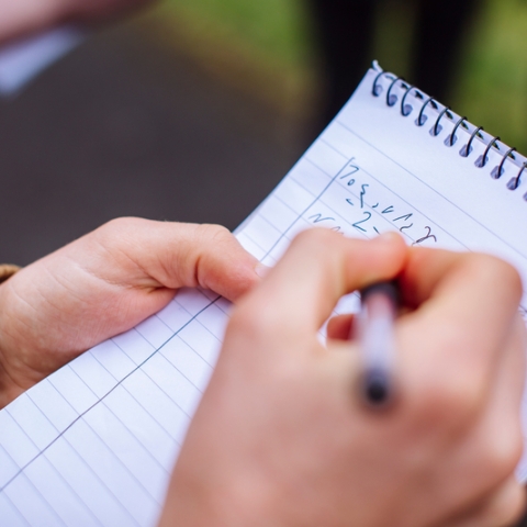 A close up of a person's hands writing shorthand on a notepad