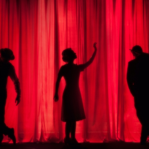 Three figures dancing in front of a red curtain