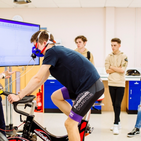 Male student training on stationary bike in front of class