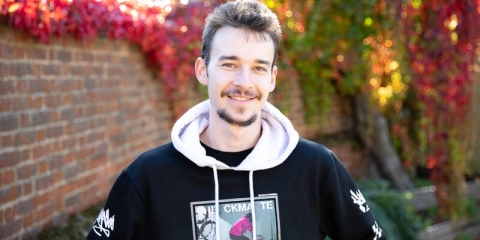 male student wearing a hooded sweatshirt standing in front of autumn trees