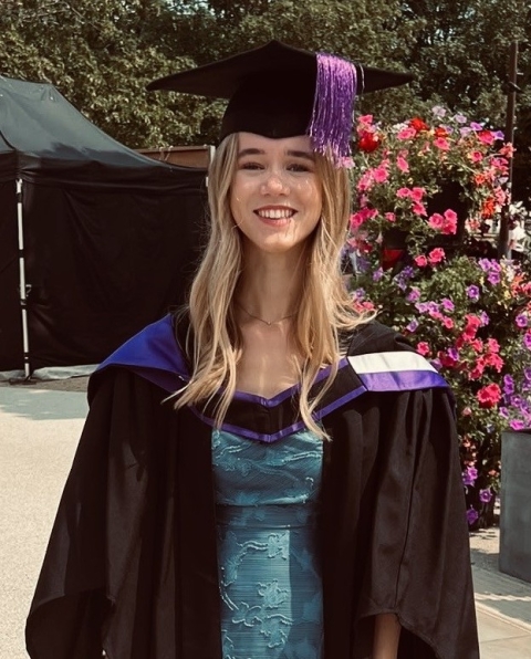 Girl with blonde wavy hair smiling in a graduation gown