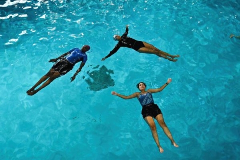 Three black female swimmers floating on their backs in a swimming pool