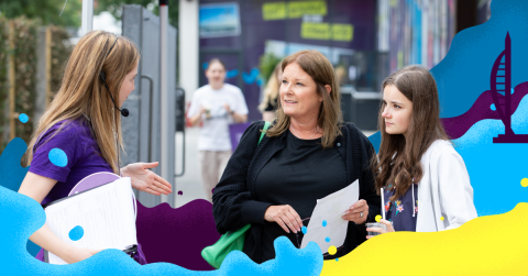 A woman and a girl listen to a female ambassador holding a prospectus 