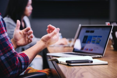 black smartphone on a desk near person holding hands up in front of laptop