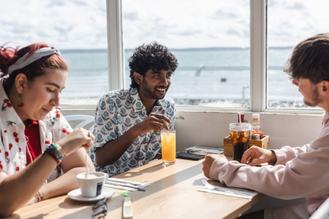Three students enjoying smoothies and coffee in a seaside café.