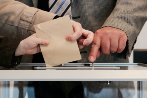 Two people placing envelopes in a ballot box