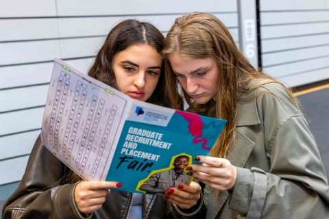 Two girls looking at the Graduate Recruitment and Placement Fair pamphlet