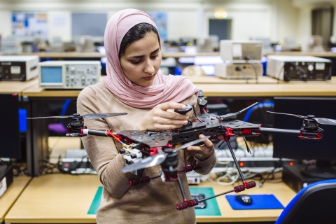 Female student wearing headscarf holding drone in lab.