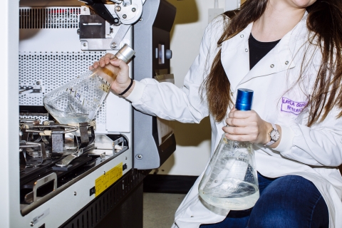 Female student in the lab putting back two beakers of clear liquid