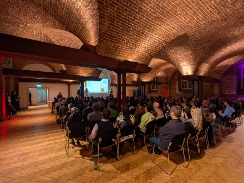 Large room with two presenters on a stage and an audience at the Inspire Future Generation Award 2025 Ceremony. 