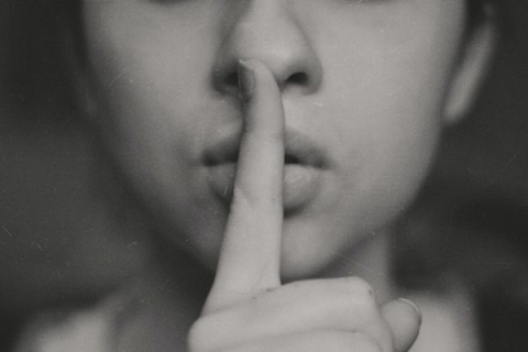 A close up photo of a person with their index finger to their lips