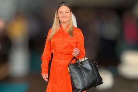 Image of Marie Oldfield holding handbag in orange dress smiling to camera