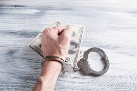 A clenched fist on top of U.S dollars with handcuffs on