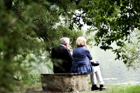 Older couple sitting on tree stump next to river.