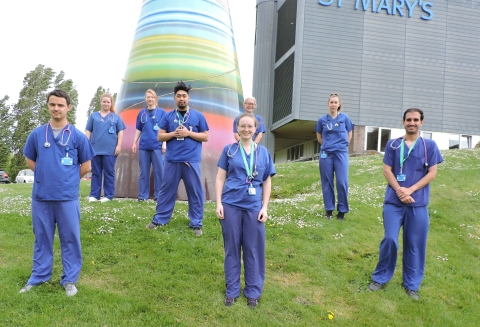 Group of nursing students wearing blue scrubs standing on grass.