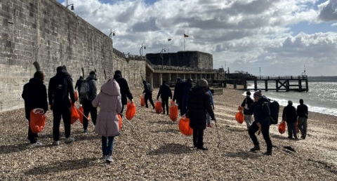 Group walking along a pebble beach carrying orange bags during a coastal clean-up.